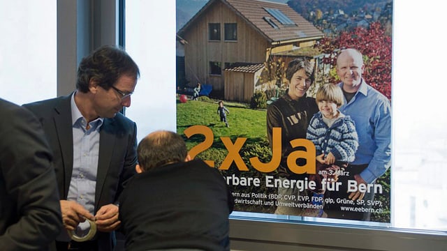 Zwei Männer kleben ein Plakat an ein Fenster. Zwei Männer kleben ein Plakat an ein Fenster.