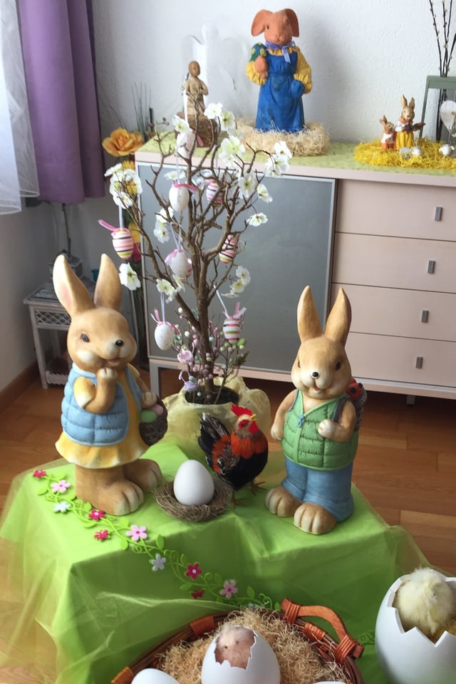 Zwei Osterhasen aus Keramik stehen neben einem Osterbäumchen das dekoriert ist.