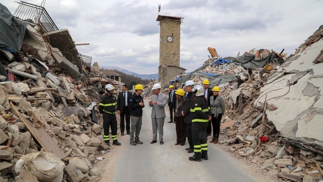 Prinz Charles umringt von anderen Männern, alle mit Helm, vor dem Kirchturm von Amatrice. Prinz Charles umringt von anderen Männern, alle mit Helm, vor dem Kirchturm von Amatrice.
