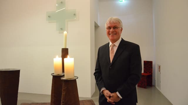 Eugen Eckert mit weissem Haar und in dunklem Anzug steht in der Stadionkapelle neben drei Kerzen. Eugen Eckert mit weissem Haar und in dunklem Anzug steht in der Stadionkapelle neben drei Kerzen.