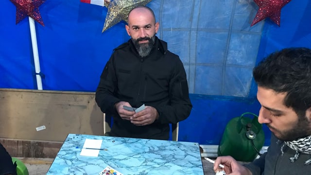 Mann, der an einem Tisch mit anderen Männern sitzt. Er hält Karten in der Hand. Mann, der an einem Tisch mit anderen Männern sitzt. Er hält Karten in der Hand.