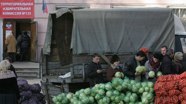 Menschen bei Gemüsekörben hinter einem Armee-Lastwagen Menschen bei Gemüsekörben hinter einem Armee-Lastwagen