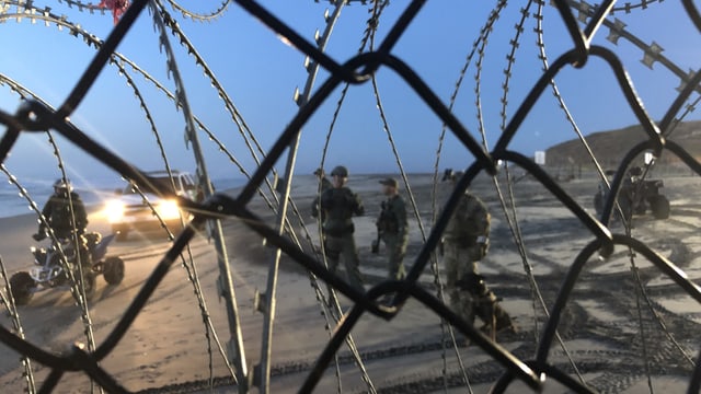 US-Soldaten überprüfen einen Migranten, fotografiert durch einen Maschendrahtzaun. US-Soldaten überprüfen einen Migranten, fotografiert durch einen Maschendrahtzaun.