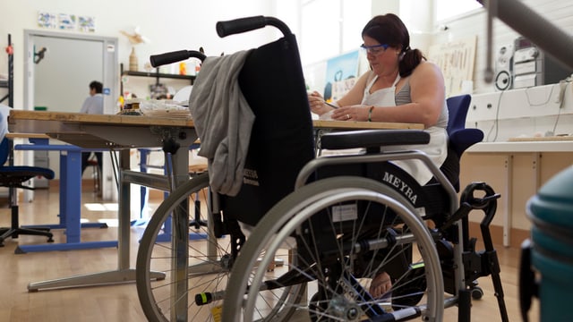 Frau an einem Tisch, daneben ein Rollstuhl Frau an einem Tisch, daneben ein Rollstuhl
