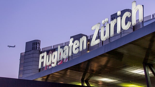 Leuchtschrift "Flughafen Zürich" an Fassade, dahinter startendes Flugzeug Leuchtschrift "Flughafen Zürich" an Fassade, dahinter startendes Flugzeug