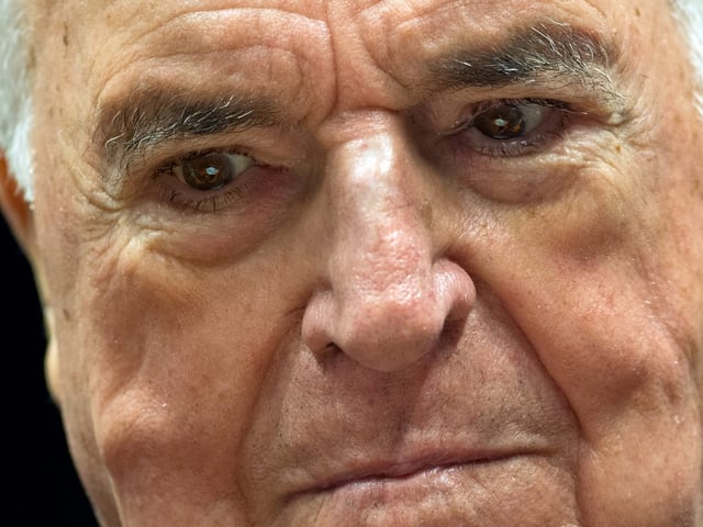 Ein sichtlich vom Alter gezeichneter Helmut Kohl blickt ernst auf den Boden. Ein sichtlich vom Alter gezeichneter Helmut Kohl blickt ernst auf den Boden.