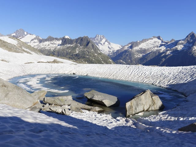 Alpine Landschaft mit Felsen, Schnee und einem kleinen Seelein.