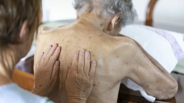 Eine Pflegefachkraft massiert einer Patientin den Rücken. Eine Pflegefachkraft massiert einer Patientin den Rücken.