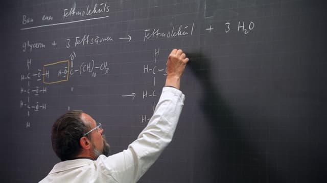 Mann in weissem Hemd schreibt mit Kreide auf eine Wandtafel. Mann in weissem Hemd schreibt mit Kreide auf eine Wandtafel.