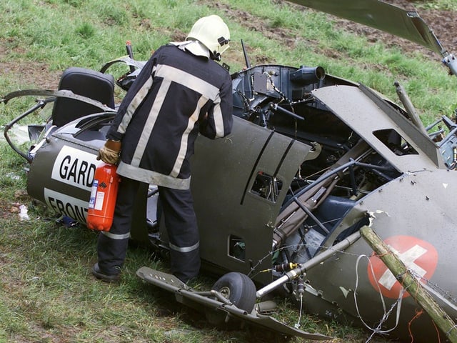 Ein Feuerwehrmann mit einem Feuerlöscher schaut in den Innenraum der zerstörten Alouette.