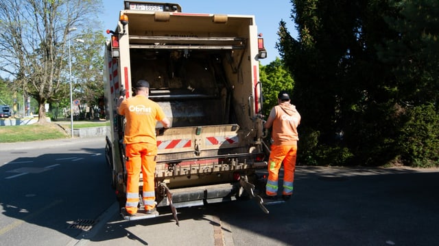 Zwei Müllmänner stehen auf der Plattform der Kehrichtabfuhr Zwei Müllmänner stehen auf der Plattform der Kehrichtabfuhr