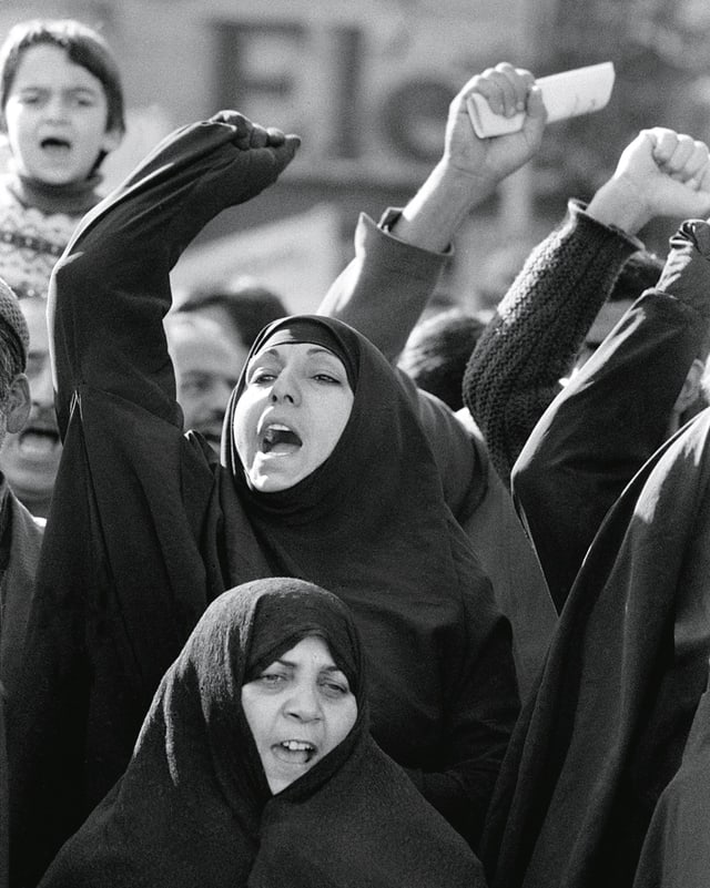 Iranische Frauen im Tschador demonstrieren mit erhobenen Fäusten.