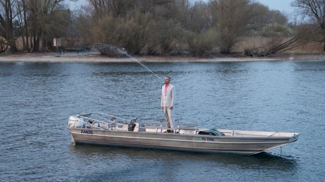 Mann in Boot stehend spuckt Wasser im hohen Bogen Mann in Boot stehend spuckt Wasser im hohen Bogen