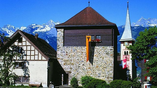 Turm des Tellmuseums in Bürglen, daneben ein Kirchturm, im Hintergrund schneebedeckte Alpengipfel. Turm des Tellmuseums in Bürglen, daneben ein Kirchturm, im Hintergrund schneebedeckte Alpengipfel.