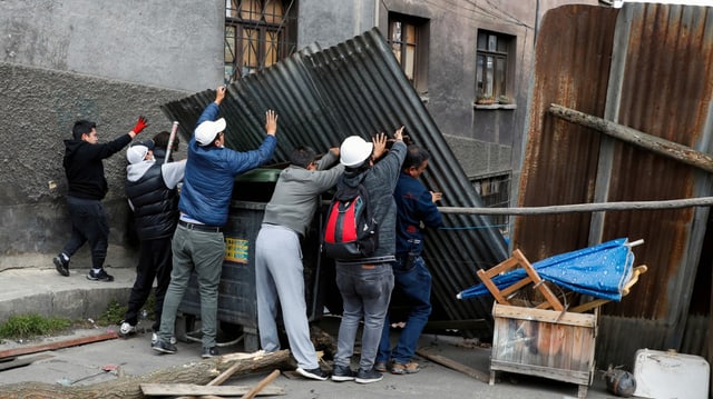 Mehrere Personen erstellen eine Wand aus Wellblech in einer Strasse. Mehrere Personen erstellen eine Wand aus Wellblech in einer Strasse.