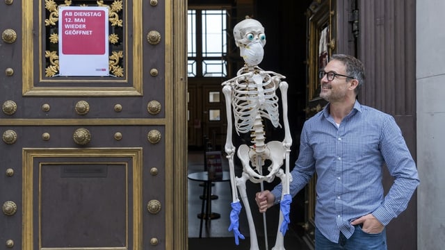 Mann mit Skelett. Das Skelett trägt Mundschutzmaske und Plastikhandschuhe. Mann mit Skelett. Das Skelett trägt Mundschutzmaske und Plastikhandschuhe.