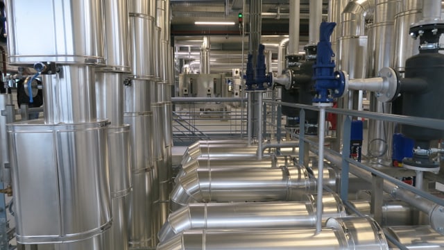 Blick in eine Fernwärme-Energiezentrale: Leitungen und Heizkessel in einer Halle. Blick in eine Fernwärme-Energiezentrale: Leitungen und Heizkessel in einer Halle.