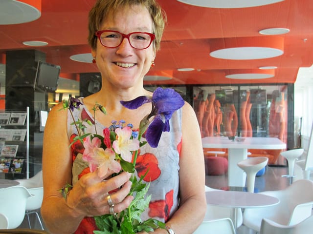 Porträt von Gärtnerin Silvia Meister mit Blumen in der Hand. Porträt von Gärtnerin Silvia Meister mit Blumen in der Hand.