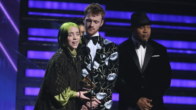Purtret da Billie Eilish e ses frar Finneas sin tribuna, Billie tegna il premi e discurra en il microfon fertant che ses frar stat dasper ella. Purtret da Billie Eilish e ses frar Finneas sin tribuna, Billie tegna il premi e discurra en il microfon fertant che ses frar stat dasper ella.