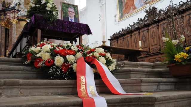 Ein rot-weisse Schleife am Kranz, der mit roten und weissen Blumen geschmückt ist. Im Hintergrund der Tisch mit dem Bild von Peter Zwick. Ein rot-weisse Schleife am Kranz, der mit roten und weissen Blumen geschmückt ist. Im Hintergrund der Tisch mit dem Bild von Peter Zwick.