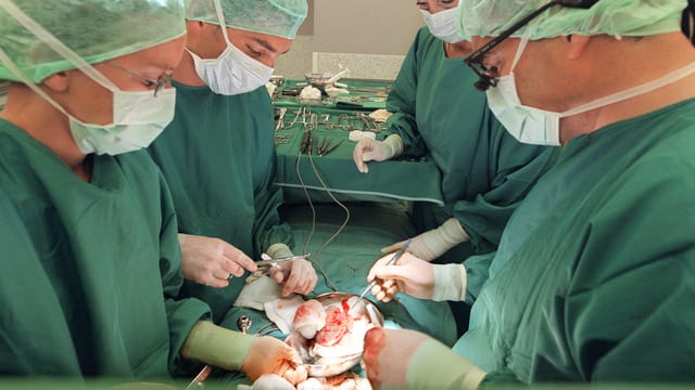 Vier Chirurgen beugen sich über Patient. 