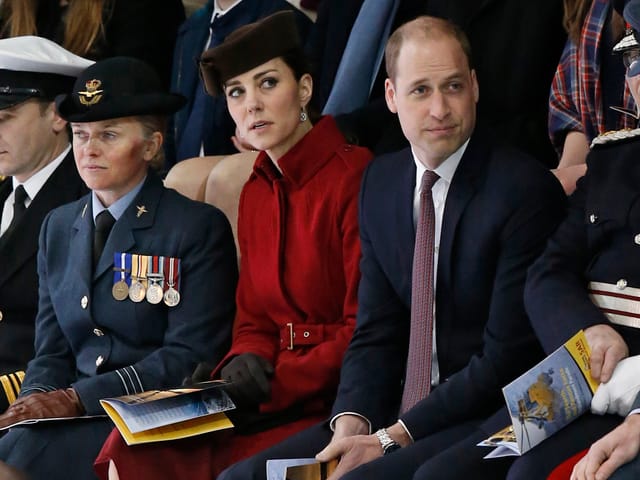 William und Kate sitzen zusammen mit anderen Menschn auf einer Sitzbank. William und Kate sitzen zusammen mit anderen Menschn auf einer Sitzbank.