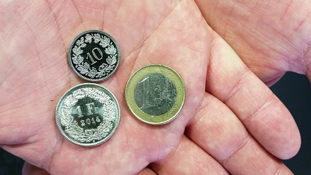 Hand hält Geldstücke: 1 Euro, 1 Franken und ein 10-Räppler. Hand hält Geldstücke: 1 Euro, 1 Franken und ein 10-Räppler.