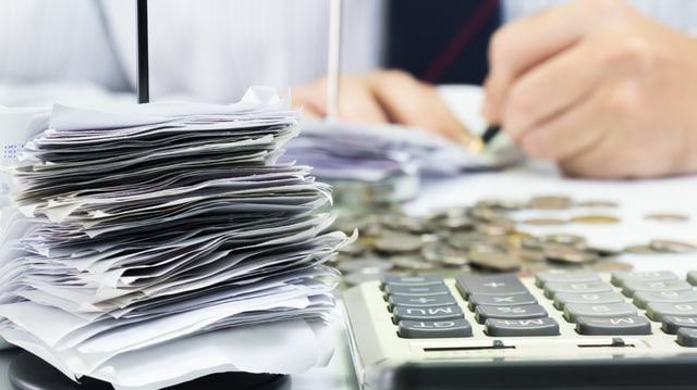 Mann füllt Unterlagen aus, Taschenrechner, Zettel und Geld auf dem Tisch Mann füllt Unterlagen aus, Taschenrechner, Zettel und Geld auf dem Tisch