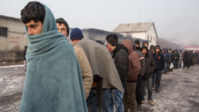 In Decken eingehüllte junge Männer stehen in der Kälte Schlange und warten auf die Essensausgabe In Decken eingehüllte junge Männer stehen in der Kälte Schlange und warten auf die Essensausgabe