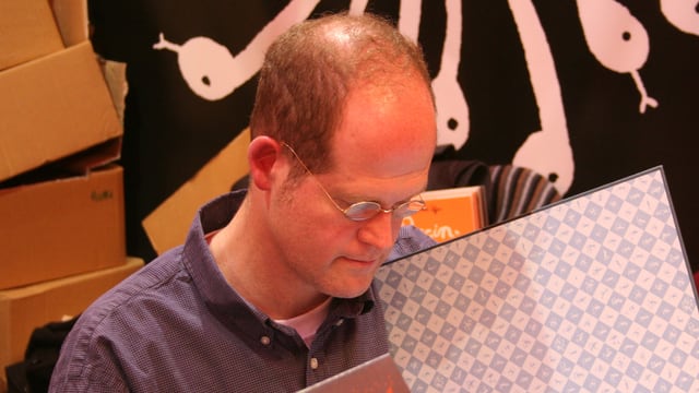 Nahaufnahme des Comic-Autors Chris Ware, während er in einem Buch blättert. Nahaufnahme des Comic-Autors Chris Ware, während er in einem Buch blättert.