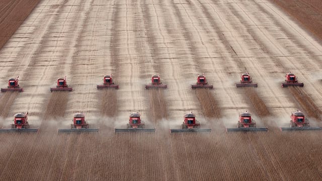 Zwei Reihen Traktoren fahren über ein Sojafeld in Brasilien Zwei Reihen Traktoren fahren über ein Sojafeld in Brasilien
