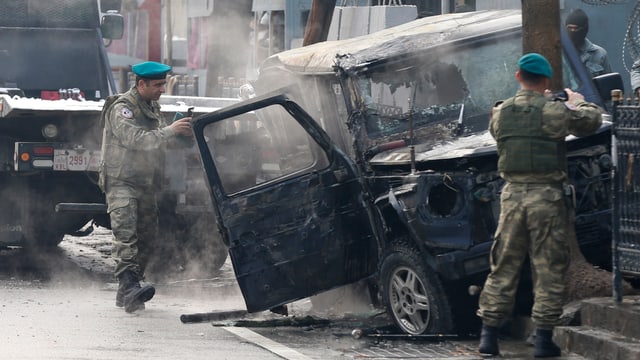 Zwei Soldaten vor einem ausgebrannten Auto. Zwei Soldaten vor einem ausgebrannten Auto.