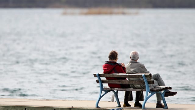 Zwei alte Menschen mit dem Rücken zur Kamera sitzen auf einer Bank und schauen aufs Wasser hinaus. Zwei alte Menschen mit dem Rücken zur Kamera sitzen auf einer Bank und schauen aufs Wasser hinaus.