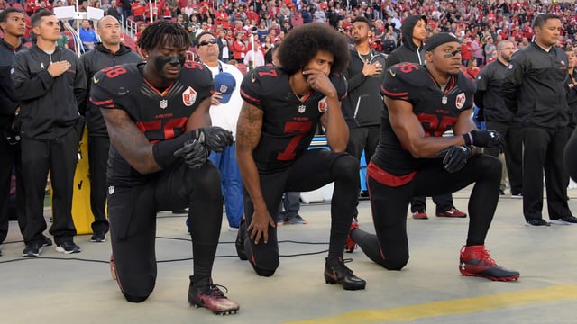 Die NFL-Spieler Eli Harold, Colin Kaepernick und Eric Reid von den San Francisco 49ers knien vor einem Spiel im Stadion. Die NFL-Spieler Eli Harold, Colin Kaepernick und Eric Reid von den San Francisco 49ers knien vor einem Spiel im Stadion.