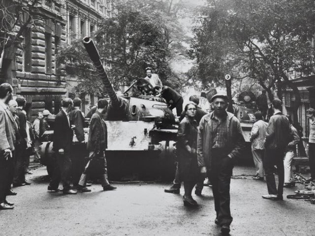 Eine Strasse mit einem PAnzer, davor PErsonen in Zivil. Eine Strasse mit einem PAnzer, davor PErsonen in Zivil.