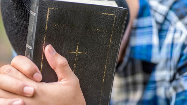 Ein Mann, der seinen Kopf nach unten hält, hat seine Hände auf einer schwarze Bibel. Ein Mann, der seinen Kopf nach unten hält, hat seine Hände auf einer schwarze Bibel.