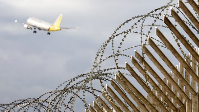 Flugzeug beim Starten, darunter ein Stacheldrahtzaun. Flugzeug beim Starten, darunter ein Stacheldrahtzaun.