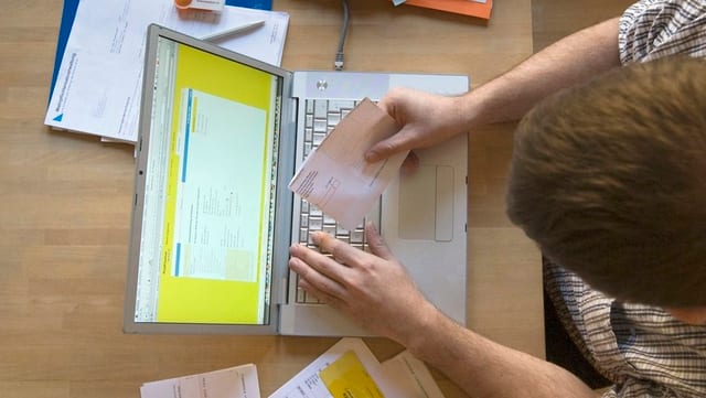 Mann von oben beim Online-Banking mit einem EInzahlungsschein an einem Mac-Computer. Mann von oben beim Online-Banking mit einem EInzahlungsschein an einem Mac-Computer.