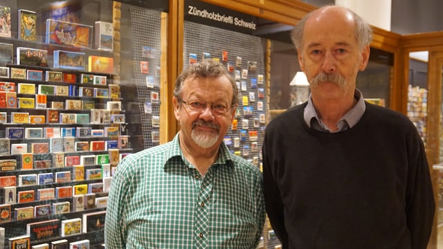Zwei Männer posieren vor den Vitrinen ihrer Austellung. Zwei Männer posieren vor den Vitrinen ihrer Austellung.