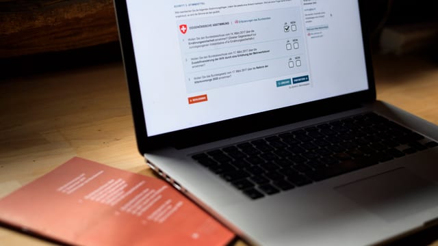 Computer mit E-Voting-Plattform, daneben Abstimmungsbroschüre des Bundes Computer mit E-Voting-Plattform, daneben Abstimmungsbroschüre des Bundes