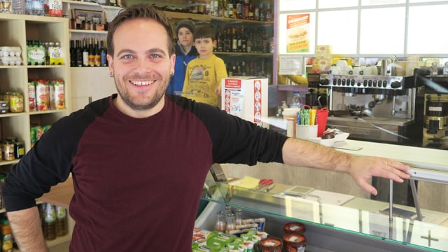 Ein Mann steht in einem Lebensmittelladen - im Hintergrund stehen zwei Kinder. 