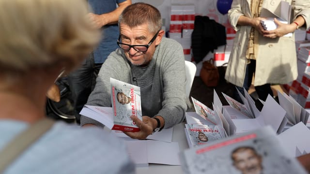 Mann hält Buch in der Hand, vor ihm Menschen Mann hält Buch in der Hand, vor ihm Menschen