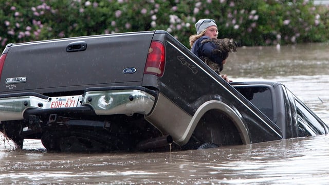 Ein Mann auf einem Auto, das im Wasser versinkt Ein Mann auf einem Auto, das im Wasser versinkt