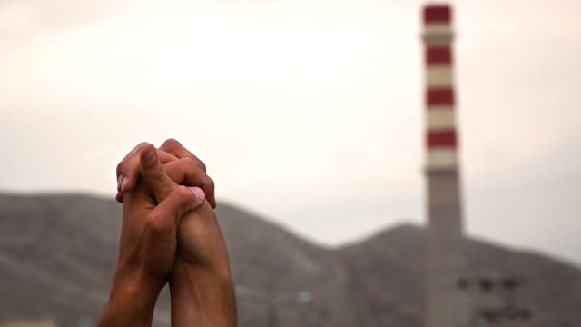 Aufnahme zweier Hände vor dem Hintergrund einer Industrieanlage. Die Hände sind gefaltet und gegen den Himmel gereckt. Aufnahme zweier Hände vor dem Hintergrund einer Industrieanlage. Die Hände sind gefaltet und gegen den Himmel gereckt.