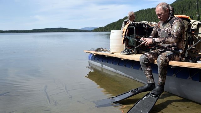 Putin sitzt auf dem Rand eines Schiffs in Taucherausrüstung. Putin sitzt auf dem Rand eines Schiffs in Taucherausrüstung.