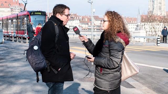 Eine Frau hält einem Mann auf der Strasse ein Mikrophon vor den Mund. Eine Frau hält einem Mann auf der Strasse ein Mikrophon vor den Mund.