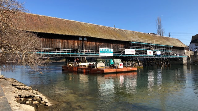 Blick auf die Holzbrücke von der Altstadt-Seite aus. In der Mitte des Bildes liegt der orange Schwimmkörper in der Aare vor der Brücke. Blick auf die Holzbrücke von der Altstadt-Seite aus. In der Mitte des Bildes liegt der orange Schwimmkörper in der Aare vor der Brücke.