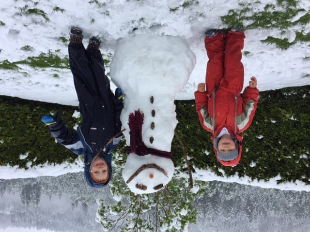 Ein Schneemann, etwa ein Meter hoch. Links und rechts davon steht je ein Kind, strahlend vor Freude.