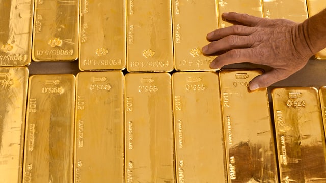 Eine Person berührt mehrere Goldbarren. Eine Person berührt mehrere Goldbarren.