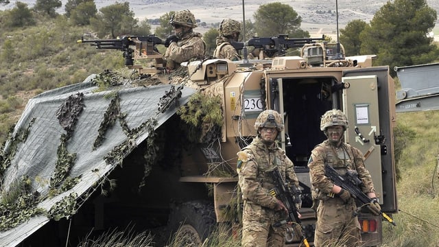 Bewaffnete Soldaten in Tarnanzügen stehen um ein gepanzertes Fahrzeug. Bewaffnete Soldaten in Tarnanzügen stehen um ein gepanzertes Fahrzeug.